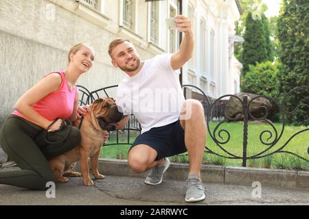 Sportliches Paar mit niedlichem Hund, der selfie draußen nimmt Stockfoto