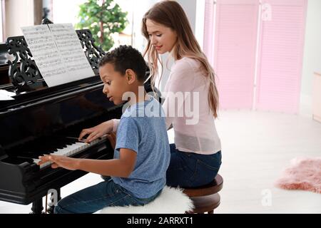 Frau, die dem kleinen afroamerikanischen Jungen beigebracht hat, zu Hause Klavier zu spielen Stockfoto