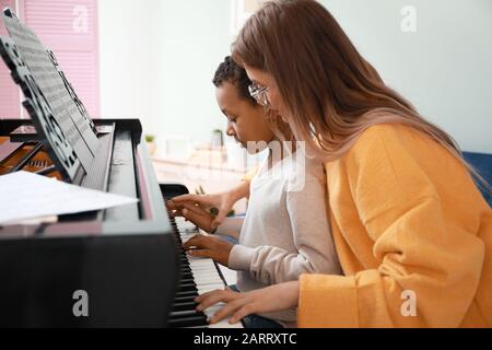 Frau, die dem kleinen afroamerikanischen Jungen beigebracht hat, zu Hause Klavier zu spielen Stockfoto