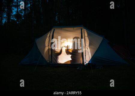 Silhouetten von Kindern, die nachts im Zelt spielen, machen Schattenpuppen mit Taschenlampe und genießen Sommerferien Stockfoto