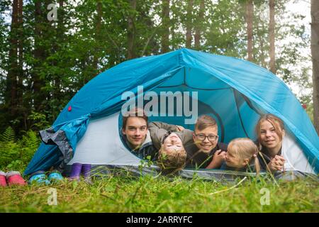 Fünf Kinder unterschiedlichen Alters liegen zusammen im Zelt im Sommerwald und genießen die Sommerferien im Freien Stockfoto