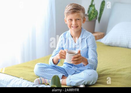 Süßer kleiner Junge, der im Schlafzimmer heiße Schokolade trinkt Stockfoto