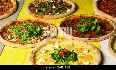 Nehmen Sie Lebensmittel mit verschiedenen Zutaten und knackigen Rändern weg. Fast Food Restaurant Konzept. Pizza kreist mit Fleisch, Pilzen, Tomaten und Käse auf gelbem Holzhintergrund. Verschiedene Pizza für die Speisekarte Stockfoto