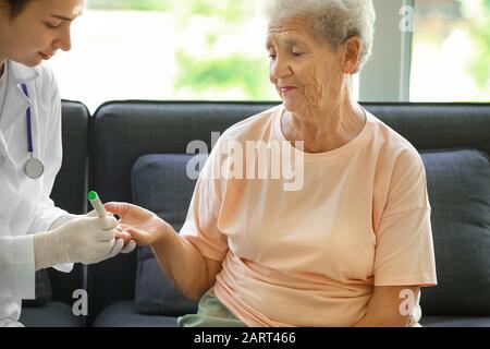 Arzt, der eine Blutprobe von Diabetikerin zu Hause nimmt Stockfoto