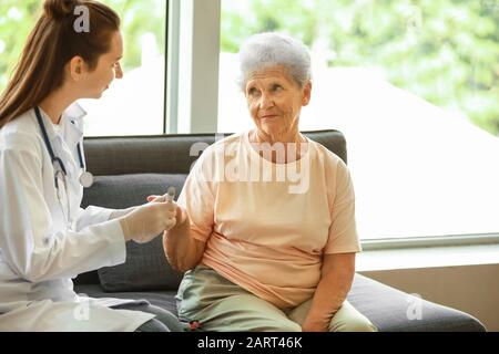 Arzt, der eine Blutprobe von Diabetikerin zu Hause nimmt Stockfoto