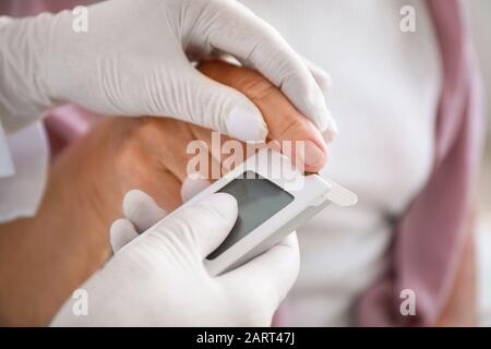 Arzt überprüft Blutzuckerspiegel von Diabetikerin zu Hause, Nahaufnahme Stockfoto