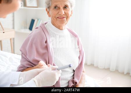 Arzt, der eine Blutprobe von Diabetikerin zu Hause nimmt Stockfoto