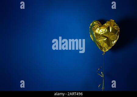 Goldene herzförmige Luftballon auf blauem Hintergrund. Zerknautschter Ballon. Geburtstag und Valentinstag Konzept. Stock-Foto. Stockfoto