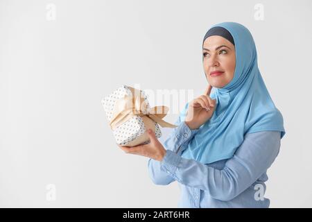 Schöne reife Muslimin mit Geschenkbox auf hellem Hintergrund Stockfoto