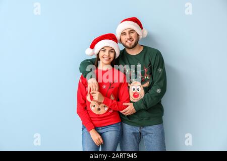 Fröhliches Paar in Weihnachts-Pullover und Weihnachtsmützen auf Farbhintergrund Stockfoto