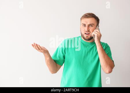 Verwirrter junger Mann, der mit dem Telefon über einen hellen Hintergrund spricht Stockfoto