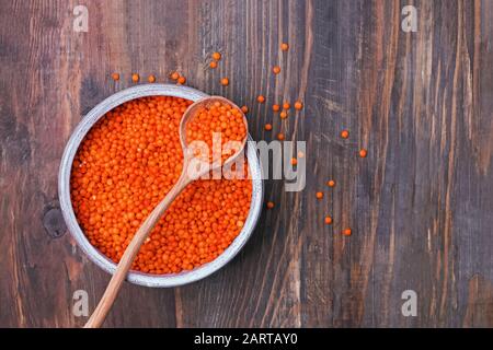 Rote Linsen in einer Schüssel und Löffel auf Holzhintergrund, Draufsicht. Stockfoto