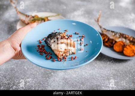 Weibliche Hand mit zubereiteten Makrelenfischen auf Platte, Nahaufnahme Stockfoto