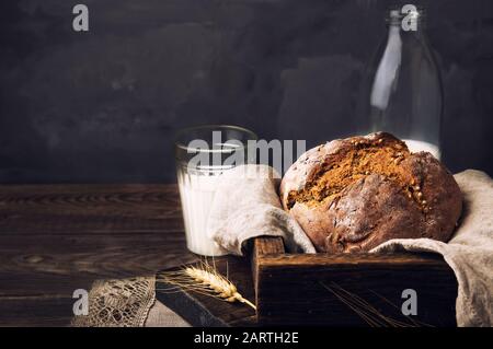 Hausgemachtes Roggenbrot mit Koriandersamen und einer Flasche Milch auf altem Holztisch. Ländliches Essen Stillleben. Stockfoto