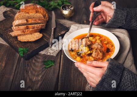 3/4-Ansicht der Frau, die Gemüsesuppe mit Fleischbällchen am rustikalen Holztisch isst. Stockfoto