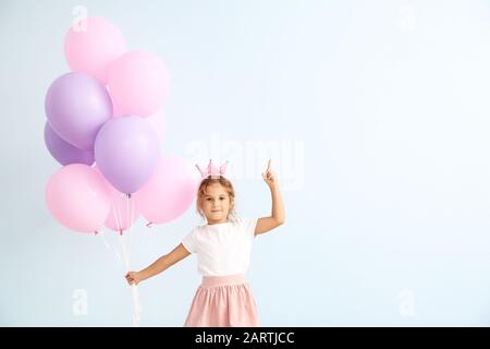 Kleines Mädchen mit Luftballons und erhöhtem Zeigefinger auf Farbhintergrund Stockfoto