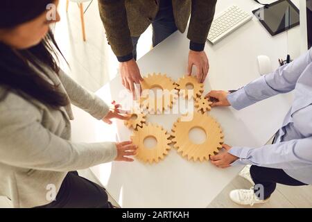 Eine Gruppe von Geschäftsleute hält Holzräder mit Zähnen in den Händen auf einem weißen Tisch im Büro. Stockfoto