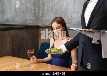 Kellner bringt Salat für junge Frau ins Restaurant Stockfoto