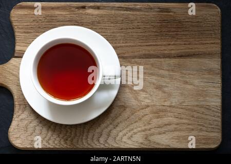 Overhead-Aufnahme von klarem Rooibos-Tee in weißer Tasse und Untertasse auf einem Holzhackbrett mit schwarzem Schiefer darunter. Stockfoto