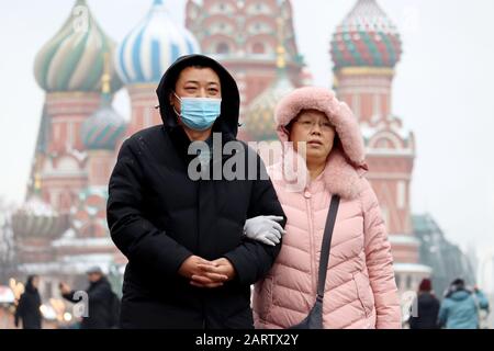 Chinesisches Paar, das auf einem roten Platz auf dem Hintergrund der St Basil's Cathedral spazieren geht. Mann in schützender medizinischer Maske, Prävention von Coronavirus, asiatischer Tourist Stockfoto