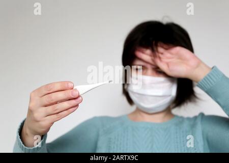 Fieber und Coronavirus Symptome, Frau misst Körpertemperatur. Besorgte Mädchen in medizinischer Maske mit Thermometer Stockfoto