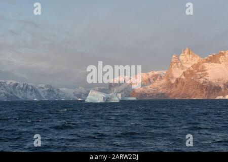 Sonnenaufgang im Fjord Scoresby Sund. Schwimmender Eisberg mit rötlich gefärbten Bergen. Kangertitittivaq, Grönland, Dänemark Stockfoto