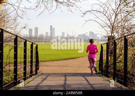 Junge Dame joggt in Hackney Marshes mit Blick auf die Skyline von London in der Nähe des Olympia Parks im Hintergrund Stockfoto