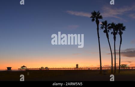 Huntington Beach Pier, romantische Aussicht mit Palmensilhouetten, Los Angeles bei Nacht Stockfoto