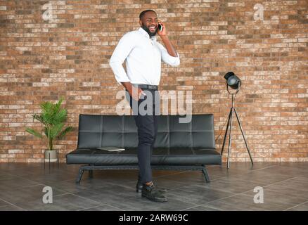 Glücklicher afroamerikanischer Geschäftsmann, der im Büro per Handy spricht Stockfoto