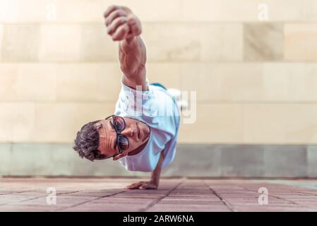 Mann im Flug, steht auf einem Arm, Superman-Pose, junge Kerltänzerin, im Sommer in der Stadt, tanzende Straßentänze, moderner Jugendstil. Mode und Fitness Stockfoto