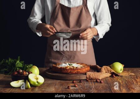 Frau streut Zuckerpulver auf apfelkuchen auf den Tisch Stockfoto