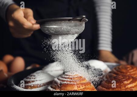 Frau, die Zuckerpulver auf Brötchen streut, in der Nähe Stockfoto