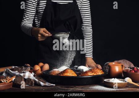 Frau, die Zuckerpulver auf die Brötchen auf dem Tisch streut Stockfoto