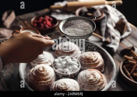 Frau, die Zuckerpulver auf Brötchen streut, in der Nähe Stockfoto