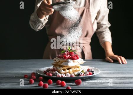 Frau streut Zuckerpulver auf belgische Wafer auf den Tisch Stockfoto