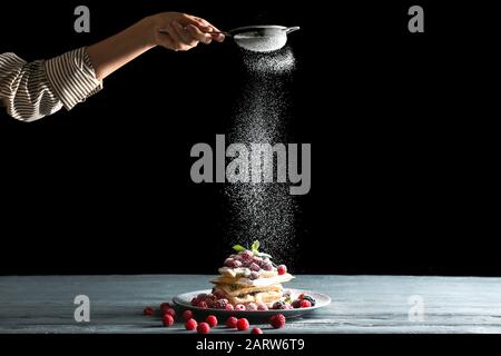 Frau streut Zuckerpulver auf belgische Wafer auf den Tisch Stockfoto