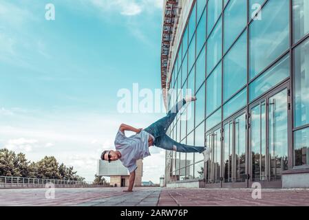 Mann steht auf einem Arm, junger Kerltänzer, im Sommer in der Stadt, tanzende Straßentänze, moderner Jugendstil. Mode- und Fitnesssport. T-Shirt Brille Stockfoto