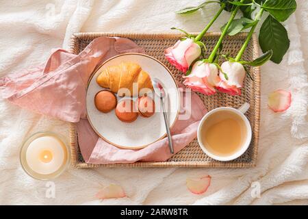 Tablett mit leckerem Frühstück und Rosenblumen im Bett Stockfoto