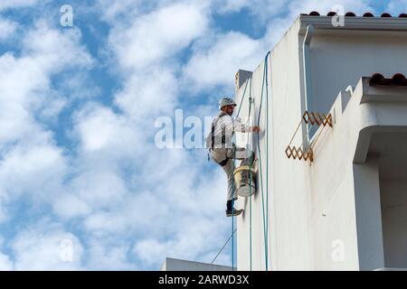 Seilzugangsabseiler, Gebäudereparaturen und Maler tragen an der Seite eines Gebäudes einen vollen Sicherheitskabelbaum Stockfoto