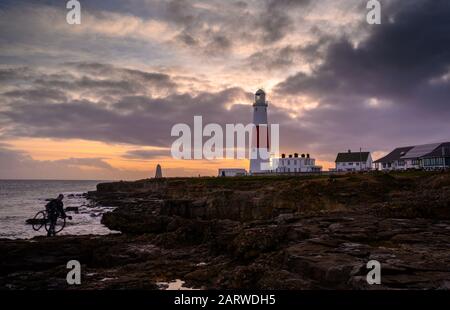 Portland Bill, Dorset 29. Januar 2020. Großbritannien Wetter: Moody Sonnenuntergang Himmel über Portland Bill. Ein Mann mit einem Fahrrad spaziert in der Nähe des South West Coast Path in der Nähe des berühmten Leuchtturms, während der Himmel vor dem Wochenende bewölkt und unruhig wird. Kredit: Celia McMahon/Alamy Live News Stockfoto