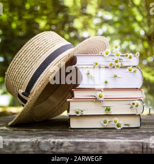 Ein Stapel Bücher auf einem alten Holztisch neben einem Strohhut eines Kanus und einem Blumenstrauß mit wilden Blumen. Stockfoto