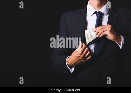 Geschäftsmann, der Bestechung vor dunklem Hintergrund in die Tasche steckt. Konzept der Korruption Stockfoto