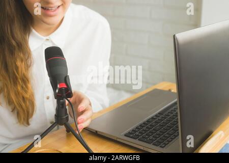 Mädchen nimmt zu Hause einen Podcast mit Mikrofon auf. Moderne Technologien zur Erstellung von Inhalten für Blogger und Einflussnehmer. Stockfoto