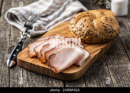 Geräucherter Schinken in Scheiben. Leckeres Schweinefleisch und Bun auf Holzschneidebrett. Stockfoto