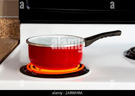 Horizontaler Schuss einer roten Pfanne kochendes Wasser auf einem Herd, wobei der Brenner zu hoch gedreht wurde. Stockfoto