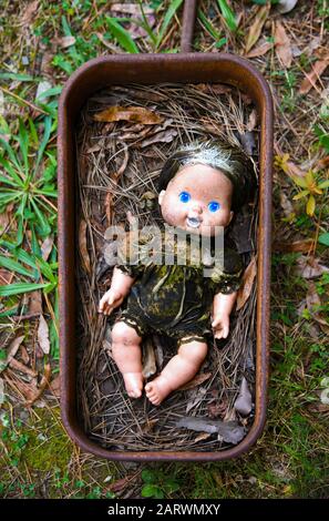 Creepy Grungy Old Baby Doll In einem Verrosteten Metal Wagon Stockfoto