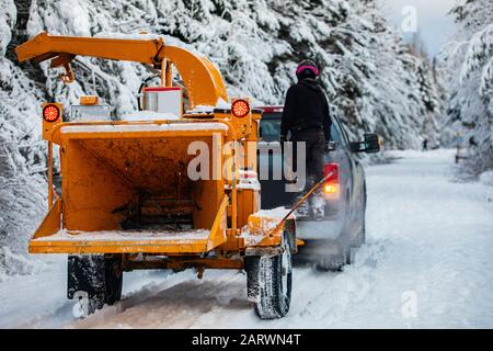 Ein Baumchirurg wird gesehen, wie er versucht, im Winter im Freien zu leben und schwere Ausrüstung durch dicken Schnee auf einer Straße im ländlichen Quebec, Kanada, zu schleppen Stockfoto