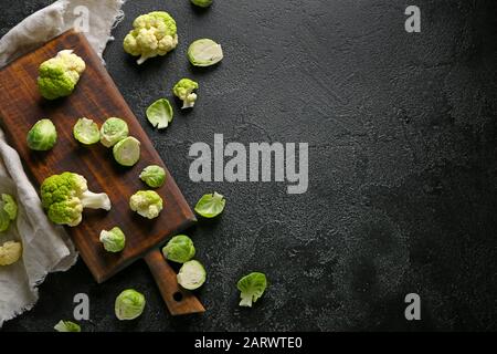 Brett mit verschiedenen frischen Kohlsorten auf dunklem Hintergrund Stockfoto