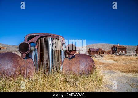 Verrostete alte Oldtimer auf gelbem Gras und braunen Häusern Im Hintergrund Stockfoto