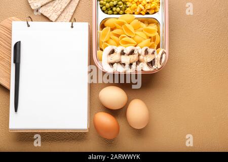 Verschiedene gesunde Lebensmittel mit Notizbuch auf Farbhintergrund. Diätplan Konzept Stockfoto